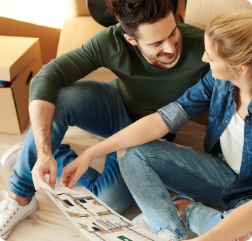 Casal feliz se olhando enquanto seguram um manual d instrução de montagem de um móvel enquanto estão em meio às caixas de mudança